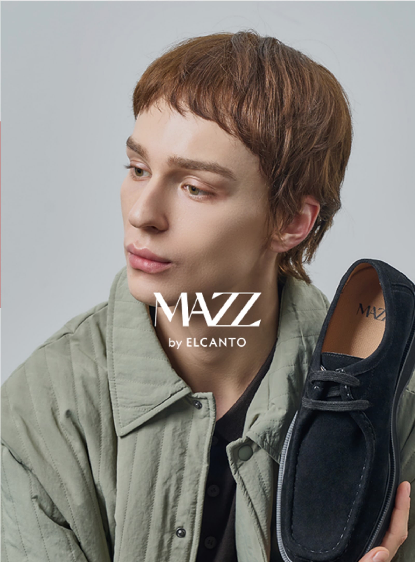 MAZZ by Elcanto campaign: a model in a quilted jacket holding a black suede lace-up shoe
